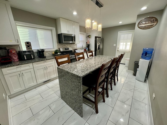 kitchen with marble finish floor, a breakfast bar area, stainless steel appliances, decorative backsplash, and white cabinets