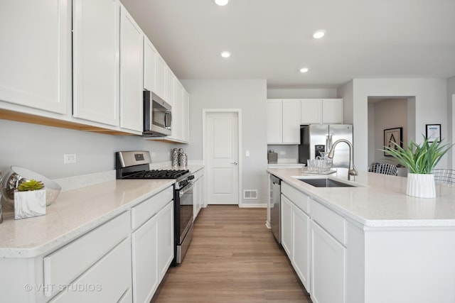 kitchen with light wood finished floors, recessed lighting, a sink, white cabinets, and appliances with stainless steel finishes