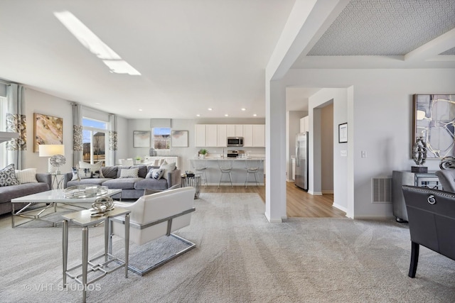 living area featuring baseboards, recessed lighting, visible vents, and light carpet