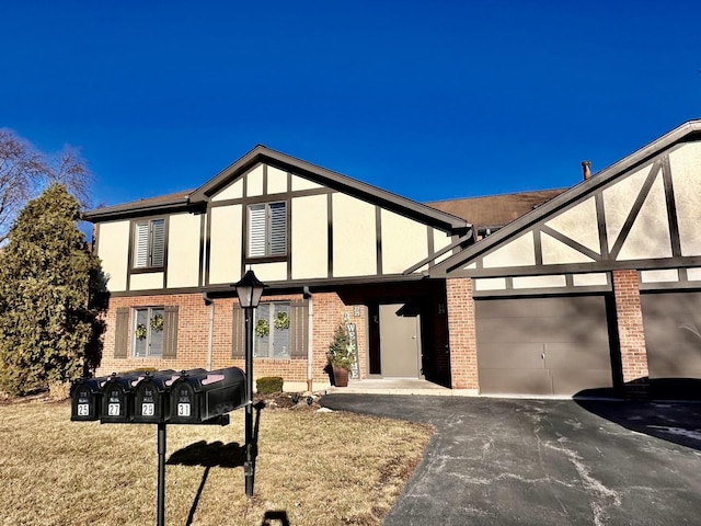 tudor home with a garage, brick siding, aphalt driveway, and stucco siding