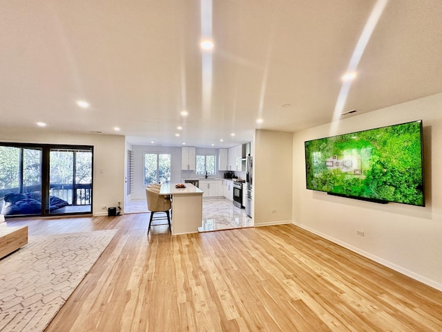 kitchen with open floor plan, light countertops, light wood-style floors, a kitchen bar, and white cabinetry