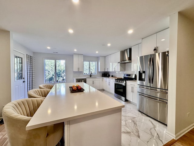 kitchen with appliances with stainless steel finishes, a center island, marble finish floor, light countertops, and wall chimney range hood