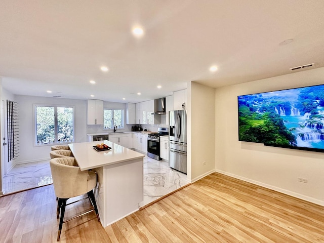 kitchen featuring stainless steel appliances, a sink, visible vents, light countertops, and wall chimney range hood