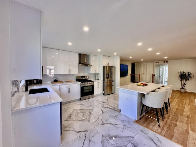 kitchen featuring a breakfast bar, appliances with stainless steel finishes, white cabinetry, a sink, and wall chimney exhaust hood