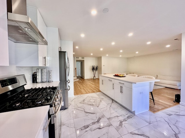 kitchen featuring a breakfast bar, marble finish floor, stainless steel appliances, white cabinetry, and exhaust hood