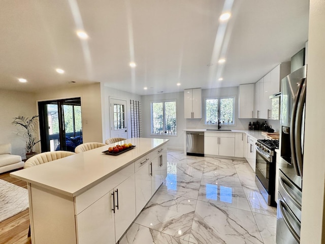 kitchen with marble finish floor, stainless steel appliances, a sink, and a kitchen breakfast bar