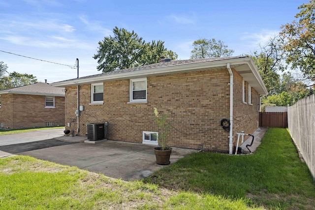 rear view of property with central AC unit, a lawn, a patio, fence, and brick siding