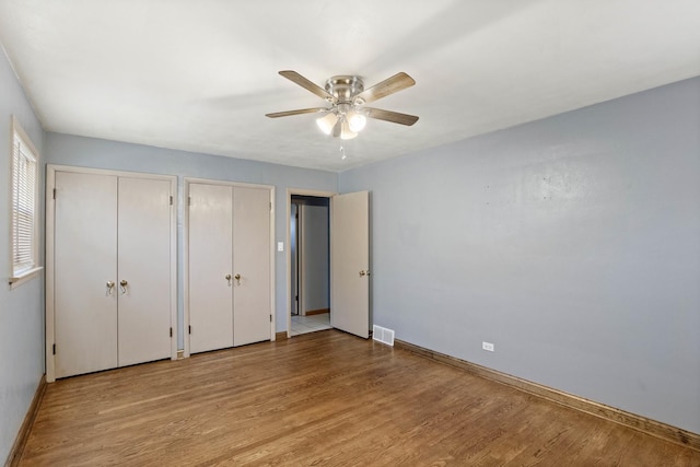 unfurnished bedroom featuring wood finished floors, two closets, visible vents, and baseboards