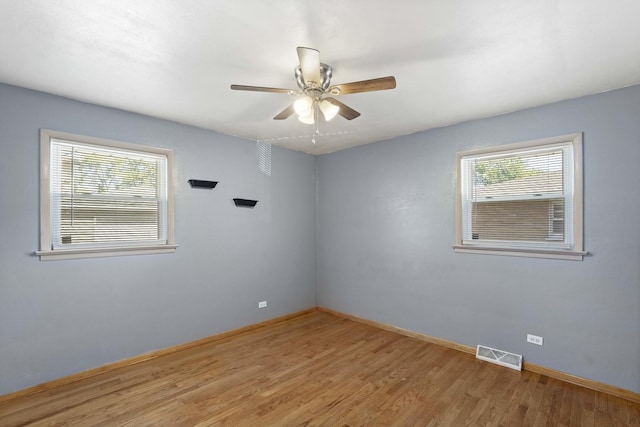 empty room featuring baseboards, plenty of natural light, visible vents, and wood finished floors