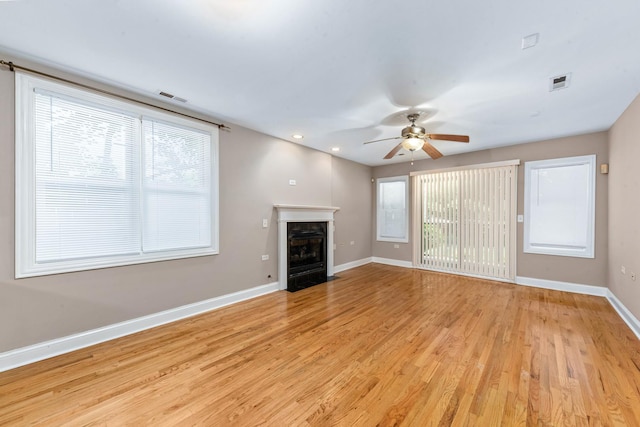 unfurnished living room with light wood finished floors, a fireplace with flush hearth, visible vents, and baseboards