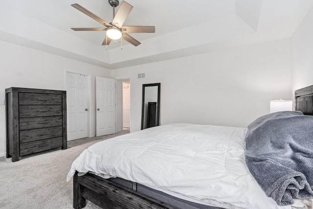 carpeted bedroom with visible vents, a tray ceiling, and ceiling fan