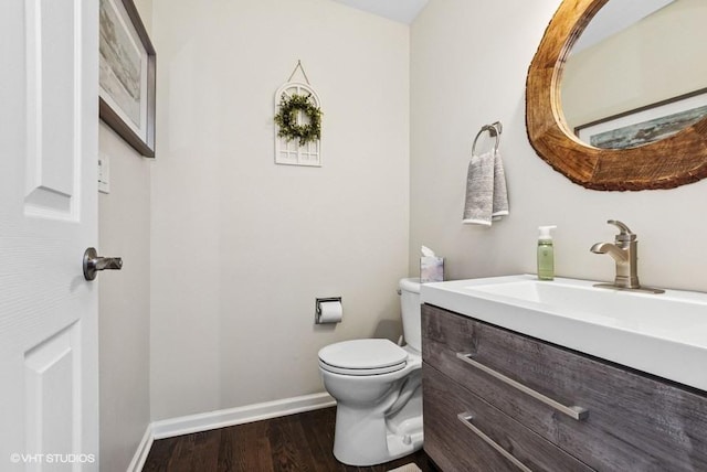 half bath featuring baseboards, vanity, toilet, and wood finished floors