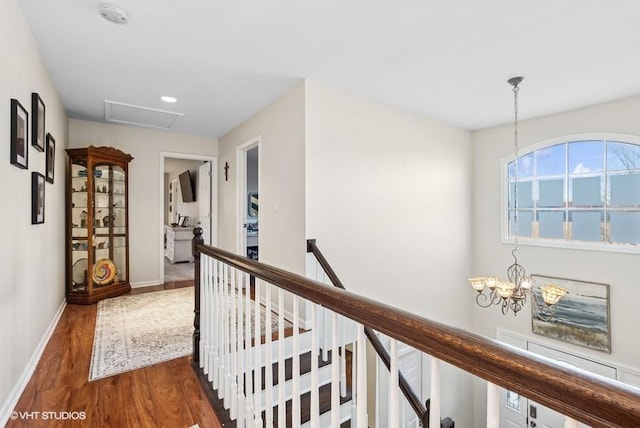 corridor with attic access, baseboards, wood finished floors, an upstairs landing, and a chandelier