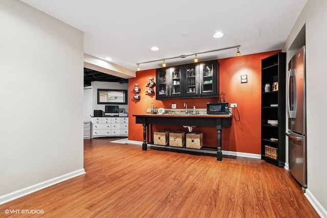 bar with baseboards, wet bar, black microwave, and wood finished floors