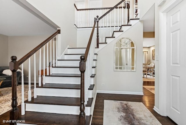 staircase with a high ceiling, wood finished floors, and baseboards