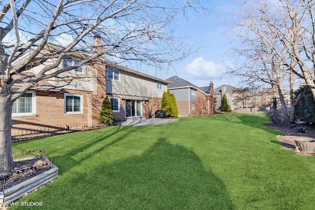 exterior space with a patio, a chimney, a lawn, and brick siding