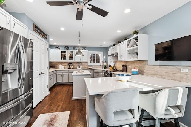 kitchen featuring a peninsula, light countertops, appliances with stainless steel finishes, a center island, and glass insert cabinets