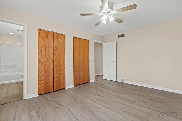 unfurnished bedroom with wood finished floors, two closets, visible vents, and baseboards