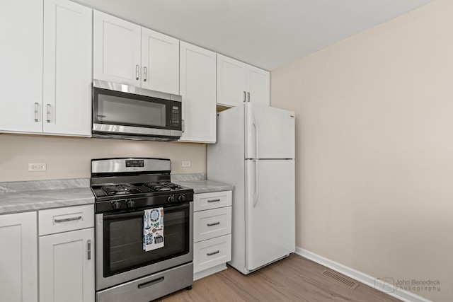 kitchen with light countertops, appliances with stainless steel finishes, light wood-style floors, white cabinets, and baseboards