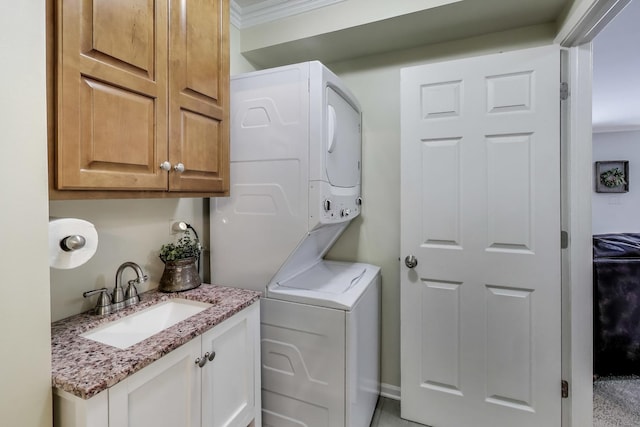 clothes washing area with stacked washer and dryer, cabinet space, a sink, and crown molding