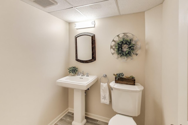 bathroom featuring baseboards, visible vents, toilet, and a drop ceiling