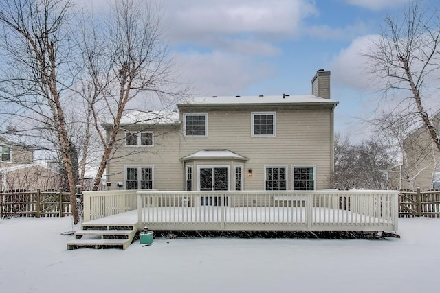 snow covered back of property featuring a deck, a chimney, and fence