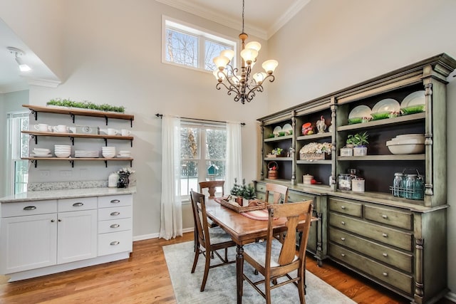 dining room featuring crown molding, a towering ceiling, baseboards, light wood-type flooring, and an inviting chandelier