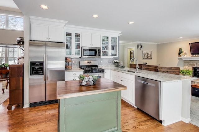 kitchen featuring appliances with stainless steel finishes, ornamental molding, a peninsula, a sink, and backsplash