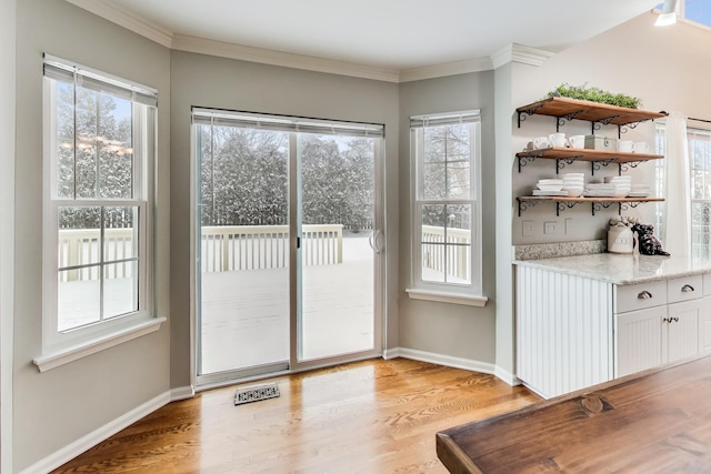 doorway with ornamental molding, light wood-style flooring, and baseboards