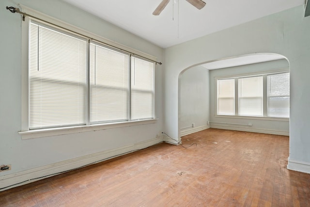 empty room with arched walkways, ceiling fan, hardwood / wood-style floors, and baseboards