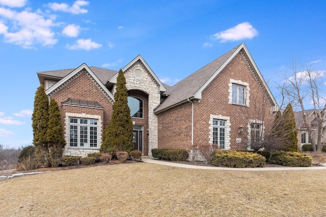 view of front of property featuring stone siding, brick siding, a front lawn, and roof with shingles