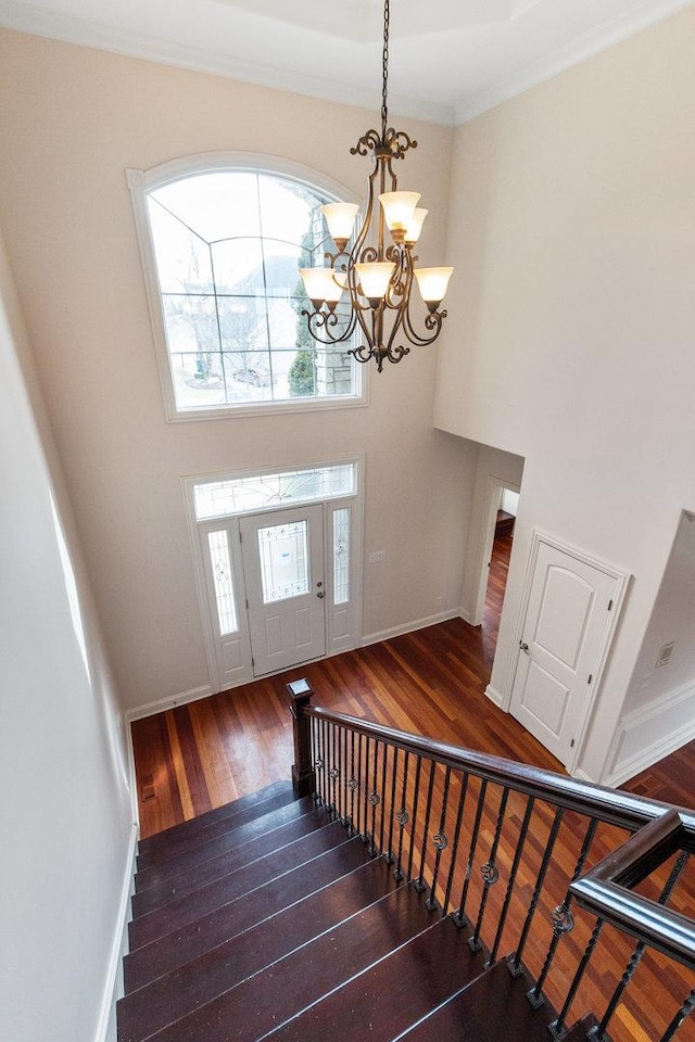 entrance foyer with a towering ceiling, baseboards, stairway, wood-type flooring, and crown molding