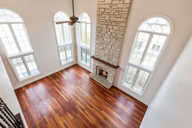 living room with baseboards, a towering ceiling, dark wood-style floors, ceiling fan, and a fireplace