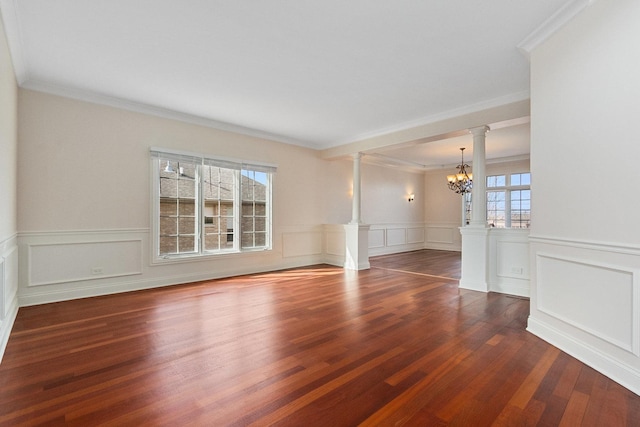 spare room with ornate columns, plenty of natural light, wood finished floors, and an inviting chandelier