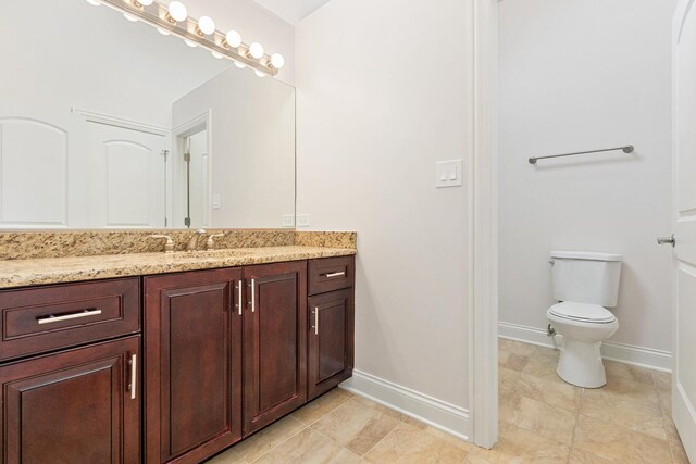 half bath featuring toilet, vanity, baseboards, and tile patterned floors