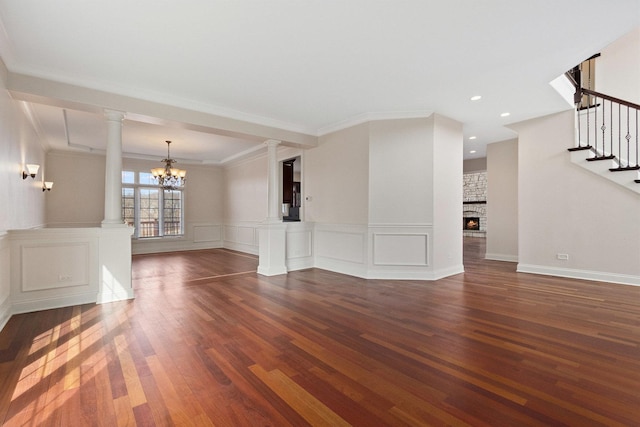 unfurnished living room featuring ornate columns, a fireplace, stairway, and wood finished floors