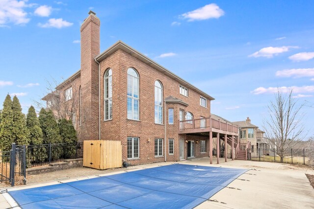 rear view of house featuring brick siding, fence, a fenced in pool, a chimney, and a patio area