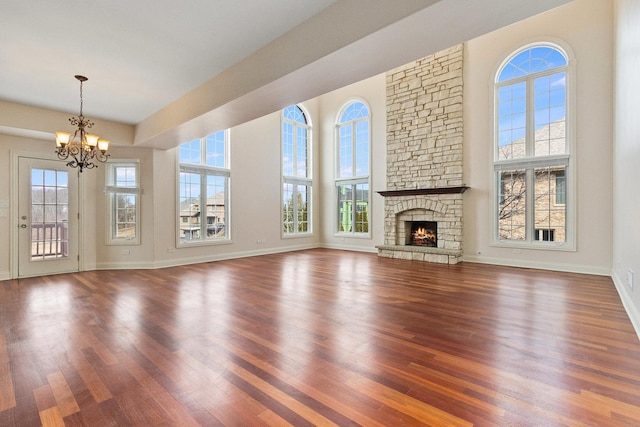 unfurnished living room with a fireplace, wood finished floors, a towering ceiling, baseboards, and an inviting chandelier