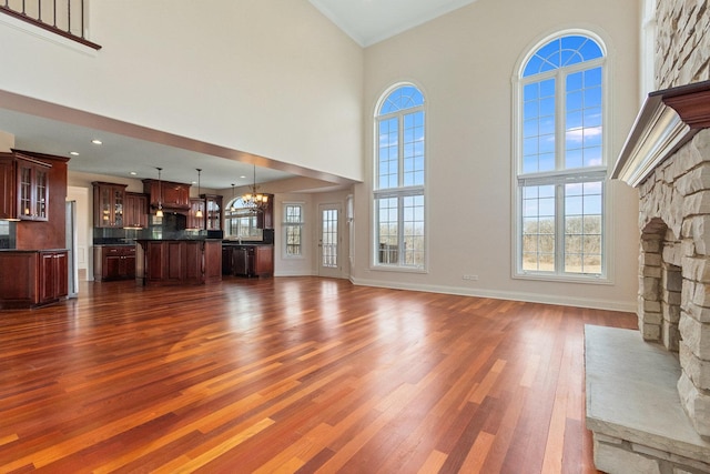 unfurnished living room with dark wood finished floors, a high ceiling, a stone fireplace, a chandelier, and plenty of natural light