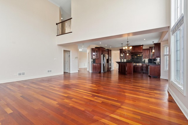 unfurnished living room with dark wood-style floors, visible vents, baseboards, and an inviting chandelier