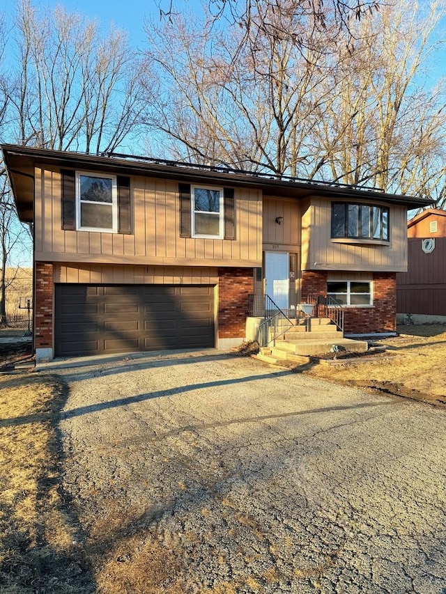 split foyer home with aphalt driveway, brick siding, and a garage