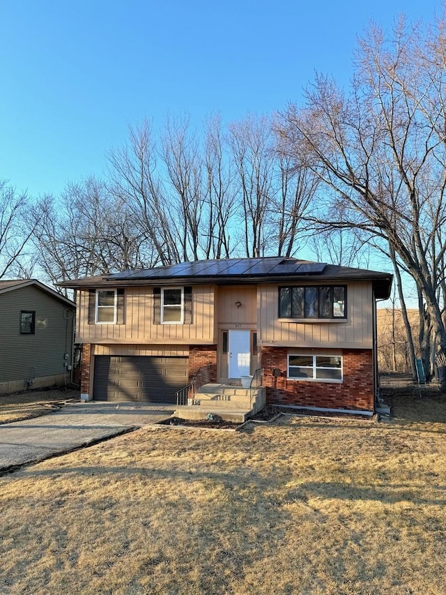 raised ranch featuring driveway, a garage, and brick siding