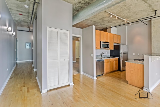 kitchen with stainless steel appliances, a sink, baseboards, light wood-type flooring, and light stone countertops