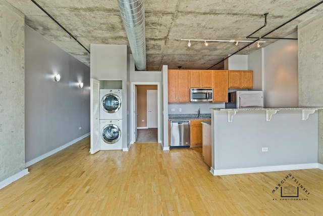 kitchen with a breakfast bar, stainless steel appliances, stacked washer and dryer, brown cabinetry, and light wood-style floors