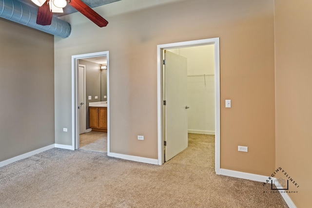 unfurnished bedroom with light colored carpet, baseboards, a spacious closet, a closet, and ensuite bath