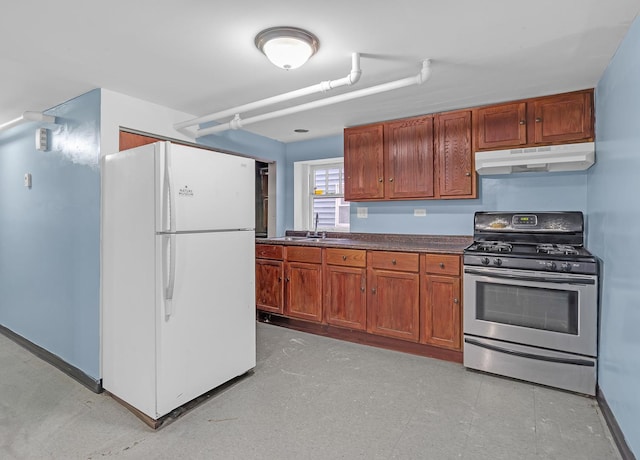 kitchen with dark countertops, gas range, freestanding refrigerator, under cabinet range hood, and a sink