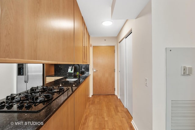 kitchen featuring light wood finished floors, stainless steel fridge, dark stone countertops, a sink, and black gas stovetop