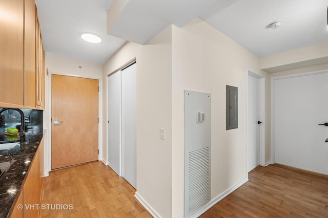 hallway featuring light wood-style floors, electric panel, a sink, and baseboards