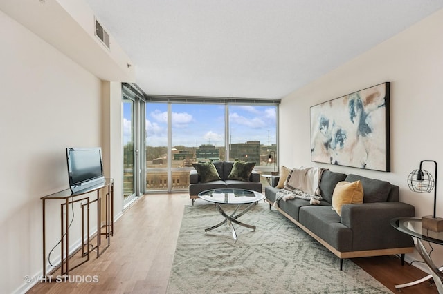 living room with baseboards, visible vents, a wall of windows, and wood finished floors