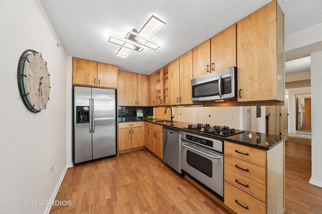 kitchen with light wood-style flooring, a textured ceiling, stainless steel appliances, and a sink